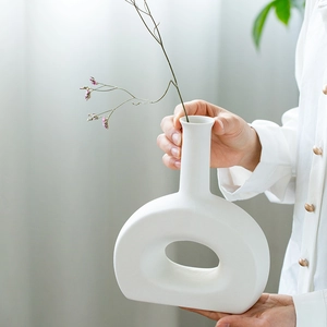 Minimalist white ceramic ring-shaped vase held by hands in a modern bright setting