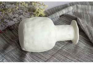 Detailed view of white ceramic vase with rough texture on a striped linen fabric