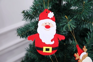 Detail of felt Santa Claus cutlery holder hanging on a green Christmas tree branch