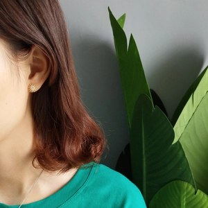 Detail of starburst gold stud earring with round zircon on ear of female model