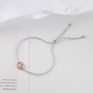 Close-up of light gray woven rope bracelet with rose gold smiley face charm