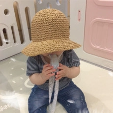 Close-up of woven straw baby sun hat with white decorative tie in a cozy indoor setting