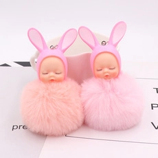 Close-up of soft plush doll keychain featuring cute sleeping baby faces and pink faux fur
