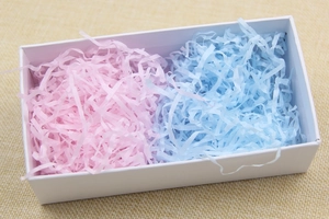 Pink and blue shredded crinkle paper filler for gift boxes displayed in a white container