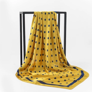 Elegant yellow polka dot silk scarf with blue border on a minimalist black stand
