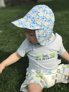 Detail of baby sun hat with neck flap featuring sun and cloud prints in outdoor grass setting