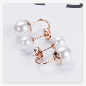 Detail of rose gold double pearl earrings with classic white pearls on white background