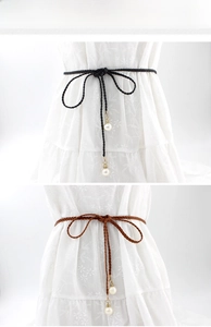 Detail of black and brown braided waist belts with pearl pendants on a white dress