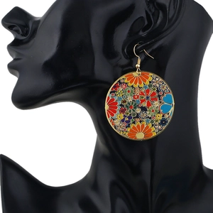 Detail of colorful enamel floral earrings on a model with gold hooks and bright patterns