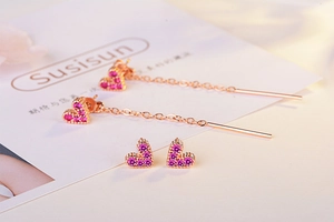 Detail of rose gold heart drop earrings and studs encrusted with pink crystals