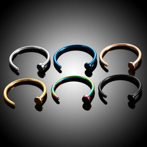 Detailed set of six colorful C-shaped stainless steel nose and lip rings on reflective surface