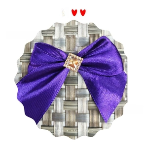Detailed view of a purple satin bow accessory featuring a square amber rhinestone centerpiece