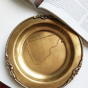 Close-up of S925 engraved tag on golden Figaro chain necklace on vintage tray