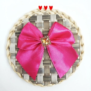 Detail of rose pink satin bow accessory featuring a square yellow crystal center on straw mat