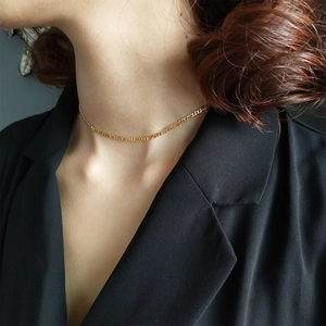 Detail of gold Figaro chain choker on model wearing a black blazer with soft lighting