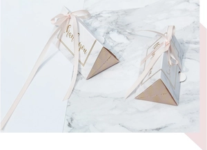 Macro detail of triangle wedding gift box with marble texture, gold foil and pink ribbon