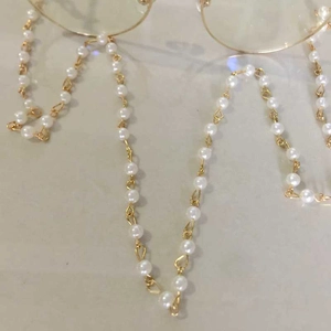 Close-up of pearl eyewear chain with golden links and sunglasses on a beige surface