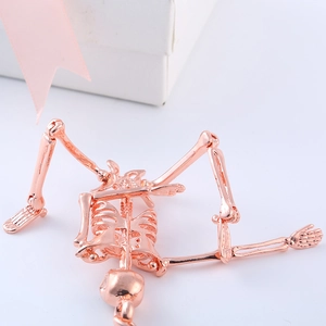 Detail of rose gold metal skull keychain lying on white surface with ribbon decoration