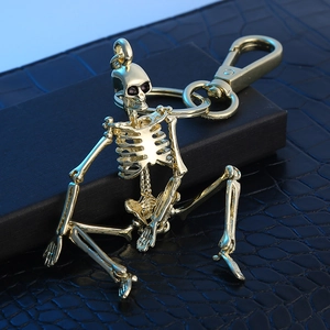 Golden skull metal keychain with spring clasp on dark crocodile leather surface