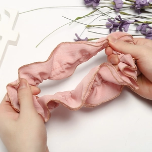 Detailed view of elastic pink fabric hair scrunchie with elegant gold trim edges