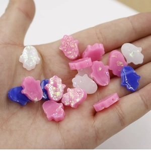 Close-up of resin Hamsa Hand beads in pink and blue held on a hand for size reference