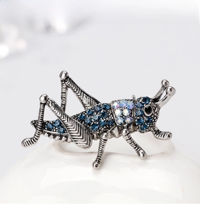 Detailed view of vintage grasshopper brooch featuring blue crystals and antique silver plating
