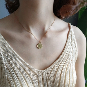 Close-up of a gold 925 silver coin pendant necklace worn on a beige knit sweater