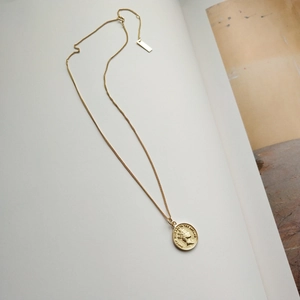 Macro detail of gold coin pendant necklace featuring Queen Elizabeth relief on white book