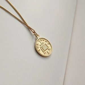 Close-up of golden penny coin pendant with one penny embossing on a minimal background