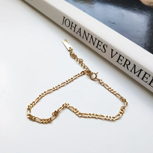 Detail of golden Figaro chain bracelet with a flat rectangular tag and spring clasp