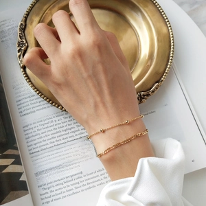 Detail of layered gold double bracelets featuring bead chain and flat Figaro link on wrist