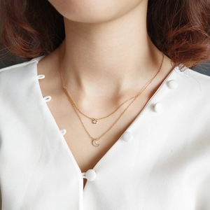 Detailed view of layered gold star and crescent moon pendant necklace on collarbone
