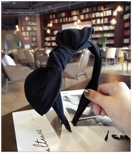 Detail of minimalist black fabric headband with oversized bow on a textured surface