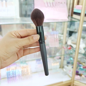 Concave foundation brush with synthetic brown bristles and black handle held in hand
