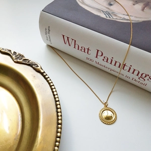 Close-up of a gold 925 sterling silver coin necklace styled with a vintage book