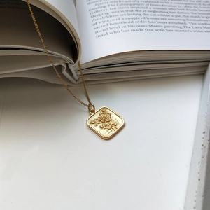 Detail of square gold rose relief pendant necklace over a vintage English dictionary