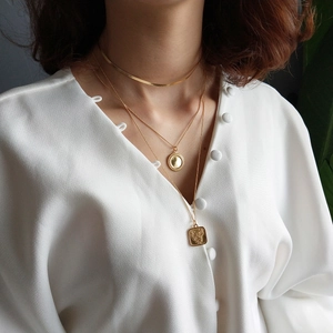 Close-up of layered gold necklaces with heart and floral pendants on a woman in a white shirt