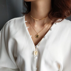 Close-up of layered gold necklaces including snake chain, round coin, and floral square pendants