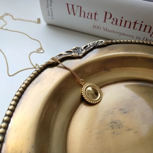 Artistic still life of gold pendant necklace on vintage tray with aesthetic book detail