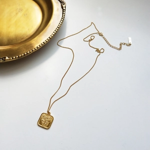 Macro view of gold square vintage pendant with floral rose relief on fine chain