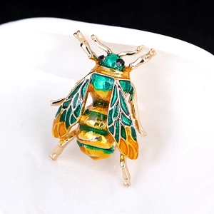 Macro detail of enamel bee brooch with green wings and gold metal texture finish