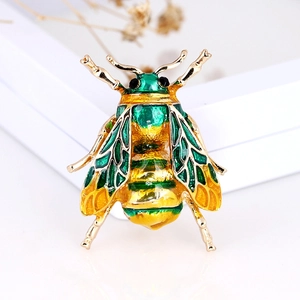 Macro detail of enamel insect bee brooch with yellow and green crystals on white surface