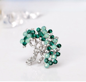 Close-up of elegant silver tree brooch with green crystal rhinestones on white background