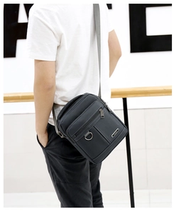 Rear side view of a black oxford fabric crossbody bag worn by a male model in a bright room
