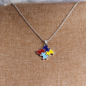 Detail of four-piece puzzle heart pendant necklace with red blue yellow enamel on brown cloth