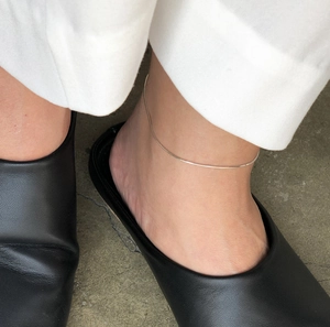Close-up of a thick silver snake chain anklet worn on the ankle with casual shoes
