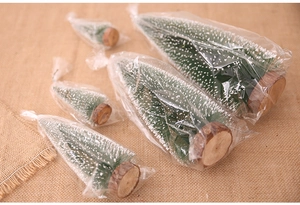 Miniature snow-dusted Christmas trees with natural wood bases on warm burlap fabric