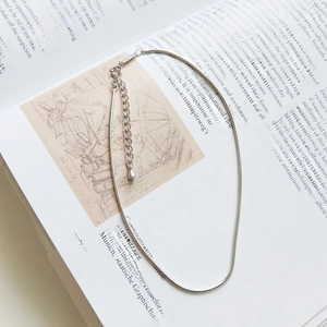 Detailed view of silver snake chain anklet with lobster clasp on an open book