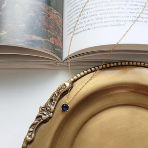 Detail of a vintage gold necklace with round blue gemstone pendant on an art book