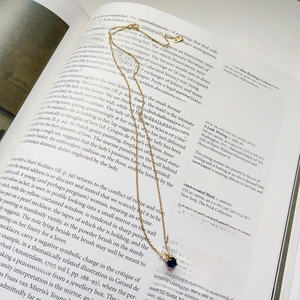 Close-up of a S925 silver gold necklace with a blue gemstone pendant on an art book